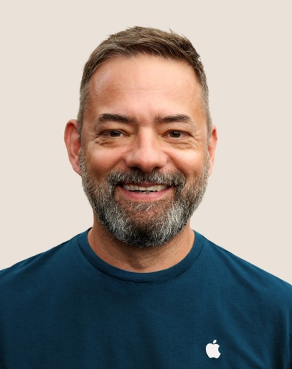 Portrait of a smiling Apple Retail team member with short gray hair and a beard.