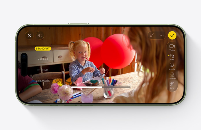 iPhone 17, önden dış görünüm, balonların olduğu bir masada oyun oynayan bir çocuğun olduğu videoda Ses Miksi özelliği kullanılıyor