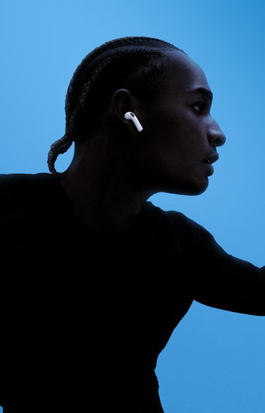 Seseorang mengenakan AirPods 5, lengan terentang, latar belakang berwarna