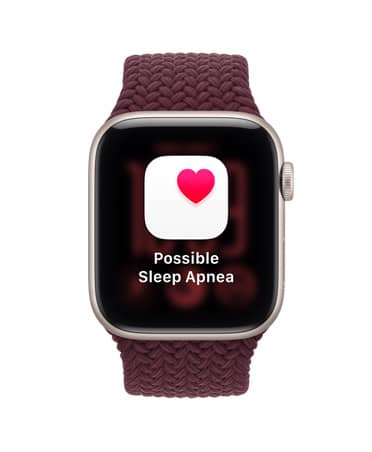 Apple Watch SE 3 z aluminiową kopertą w kolorze księżycowej poświaty i plecioną opaską sportową w kolorze burgunda. Ekran wyświetla powiadomienie o możliwym bezdechu sennym. Na prawym boku urządzenia pokrętło Digital Crown