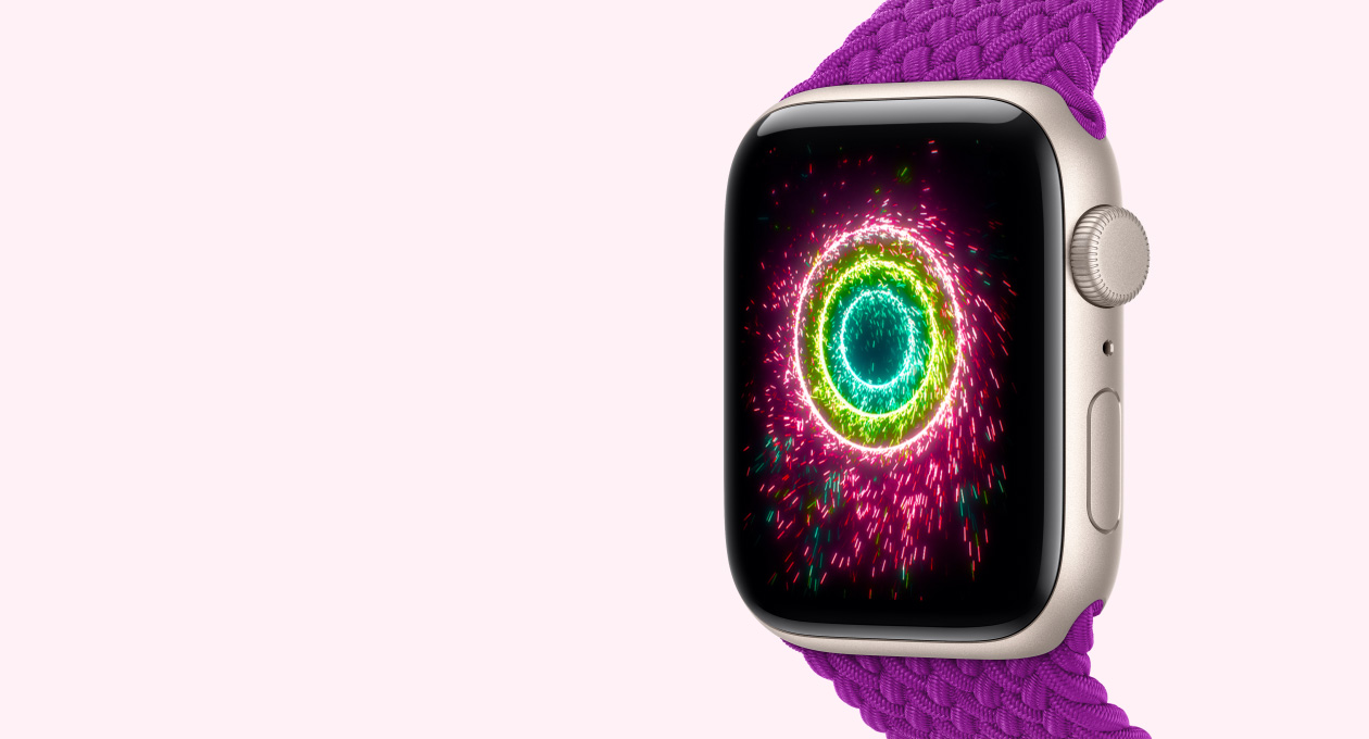 Apple Watch SE 3, caja de aluminio color blanco estrella, con correa Solo Loop trenzada color magenta, la pantalla muestra los anillos de Actividad con diseño de bengalas, anillos concéntricos rosa, verde lima y azul claro
