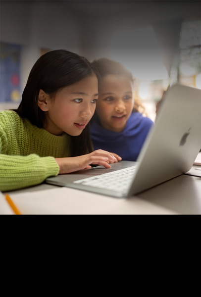 Kaksi nuorta opiskelijaa istuu pöydän ääressä ja katsoo keskittyneesti MacBookia työskennellessään yhdessä luokkahuoneessa