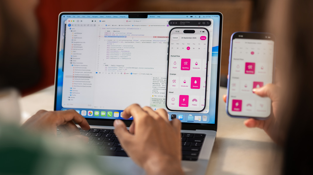 Xcode를 실행 중인 MacBook에 타이핑하고 있는 사람의 어깨 너머에서 본 모습. 누군가 Sakhi 앱이 표시된 iPhone을 들고 있고, MacBook에도 Sakhi 앱이 표시되어 있습니다.