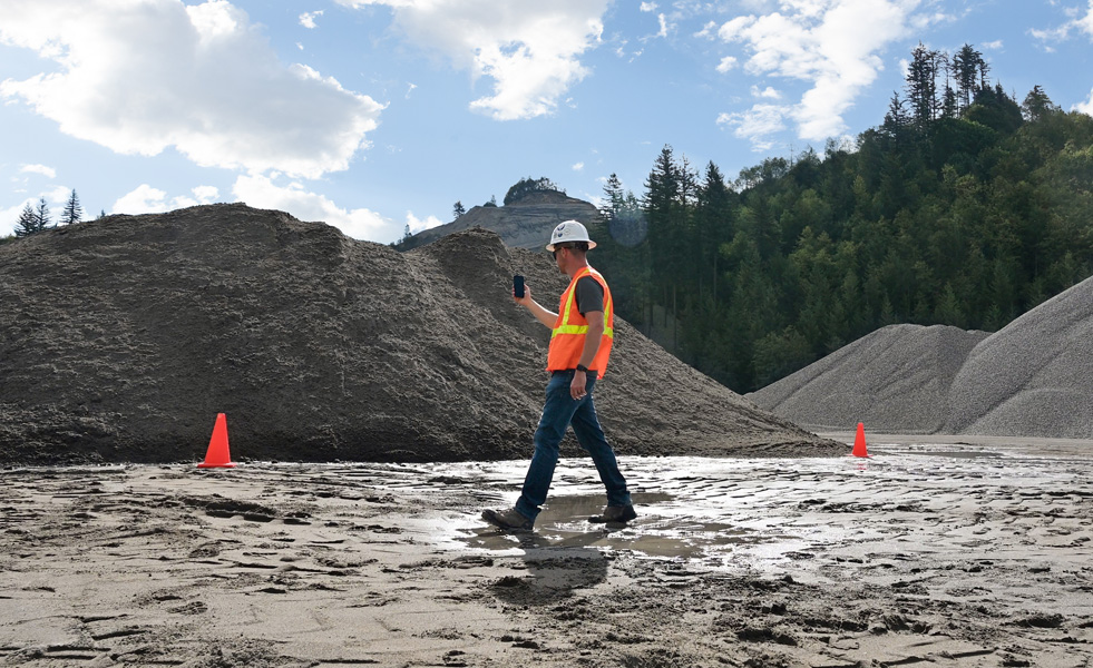 A field worker uses an iPhone to assess a worksite while walking across muddy terrain