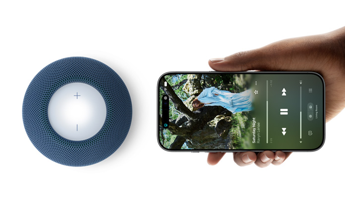 HomePod mini 2 og iPhone: En hånd holder en iPhone vandret ved siden af en blå HomePod mini 2 for at demonstrere funktionen Handoff