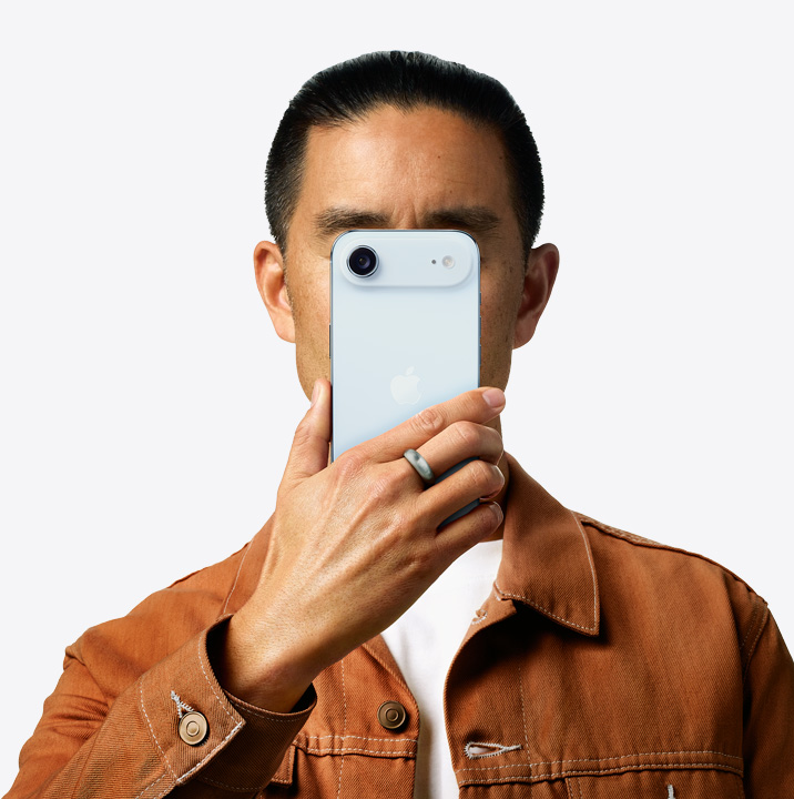 امراة تحمل iPhone16 باللون الوردي أمام وجهها ويظهر الجزء الخلفي الخارجي، ونظام الكاميرا المزدوجة في الزاوية العلوية اليسرى.