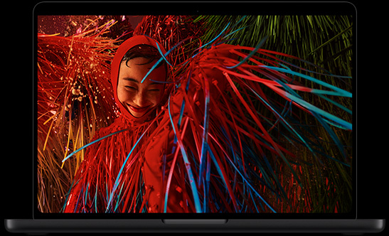 Åben MacBook Pro med PROLED XDR-skærm, farven er space black, skærmen viser et billede af en smilende person i et surrealistisk rødt outfit med fjeragtige detaljer
