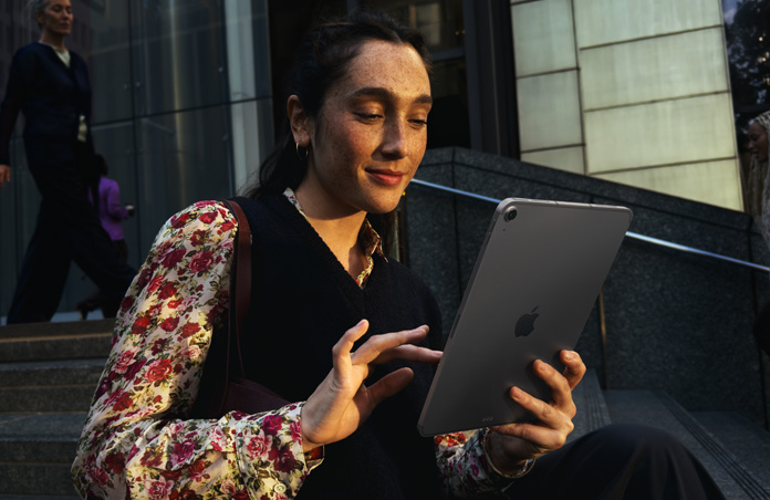 Une personne assise sur des marches devant un grand bâtiment utilise un iPad Air 11 pouces gris sidéral, avec une connexion Wi‑Fi constante pendant les transferts de données réseau