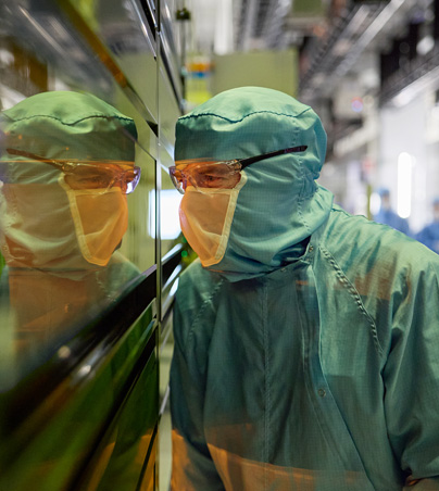 An employee in full-body work suit peers into a window of a semiconductor machine